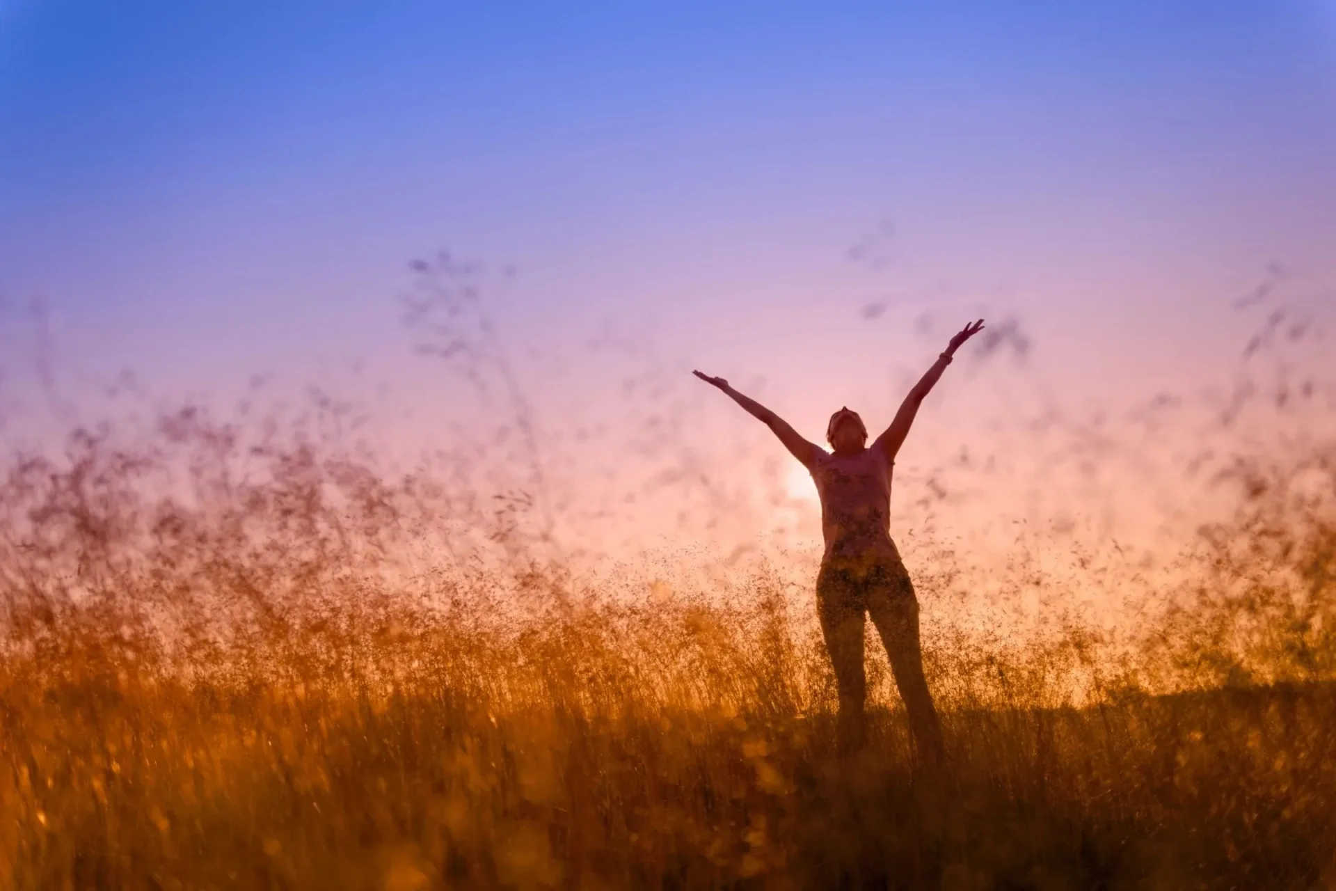 A woman standing in the grass with her arms raised.