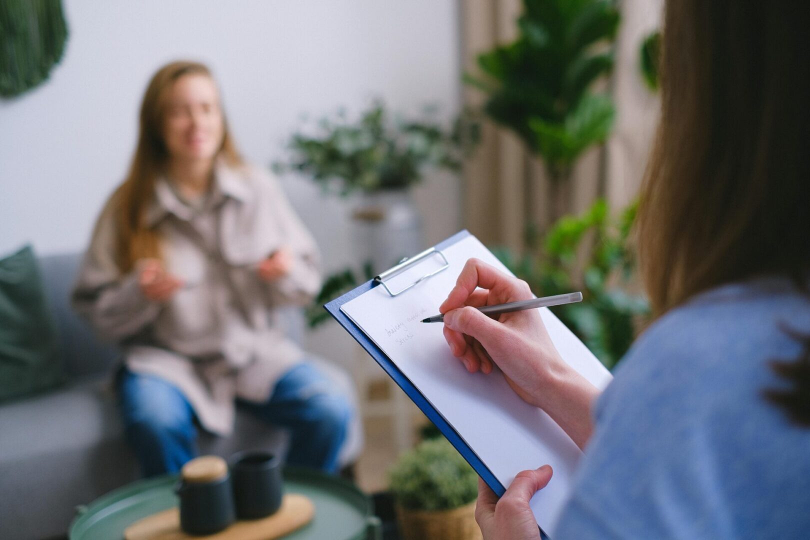 A person writing on paper near another person.